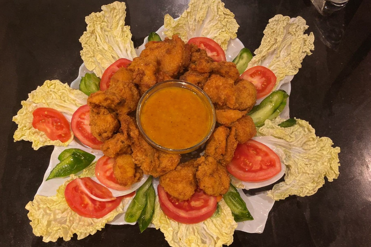 Crispy fried prawns arranged over a fresh salad with tomatoes and lettuce, served with dipping sauce