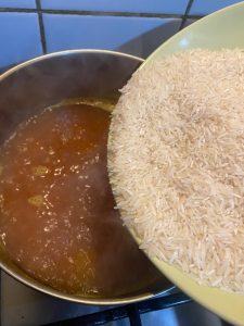 Raw rice being added to a pot of boiling turmeric water on the stove.