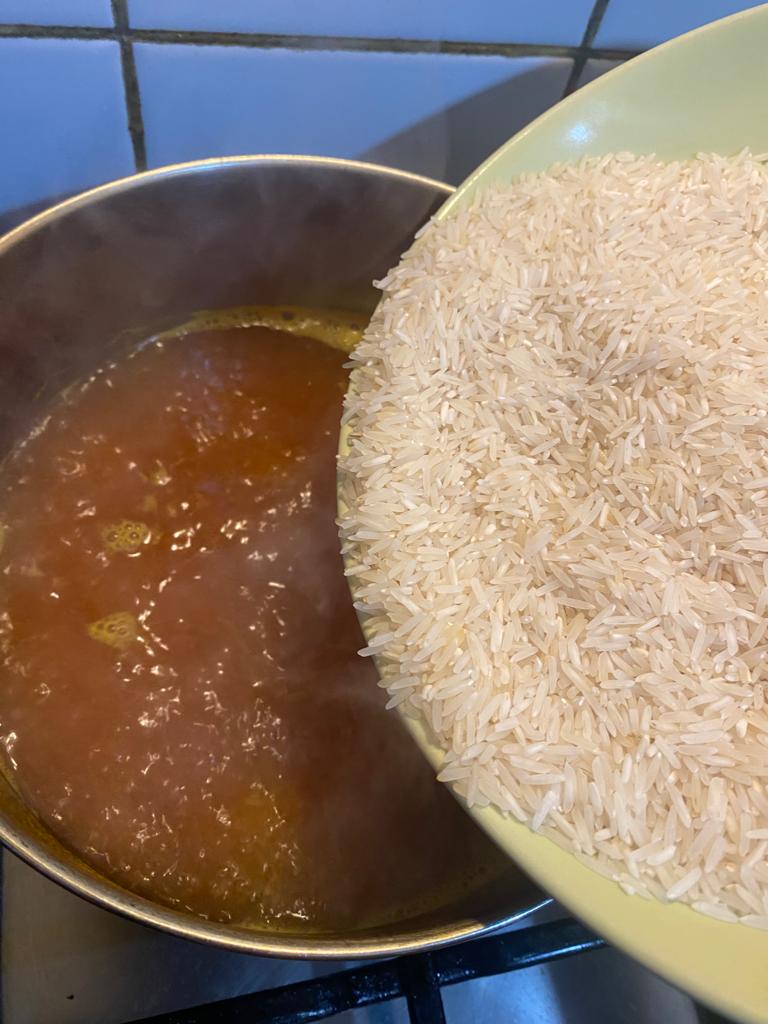 Raw rice being added to a pot of boiling turmeric water on the stove.