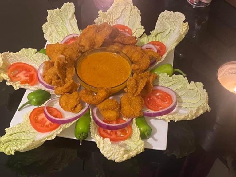 A beautifully arranged platter of crispy fried prawns with dipping sauce, surrounded by fresh lettuce leaves, tomato slices, onion rings, and green peppers