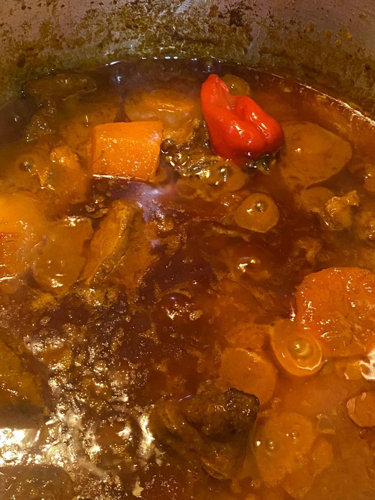 Lamb and beef stew simmering with carrots, vegetables, and a whole Scotch bonnet pepper.
