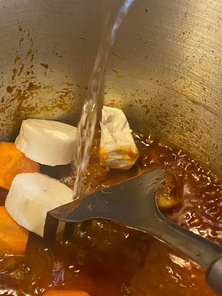 Cassava and carrots simmering in rich tomato stew with water being added