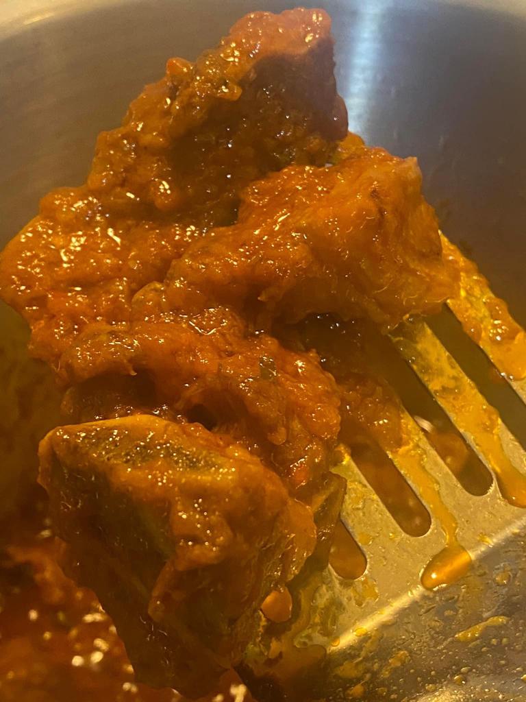 Beef chunks coated in thick tomato paste sauce are lifted with a slotted spatula in a cooking pot.