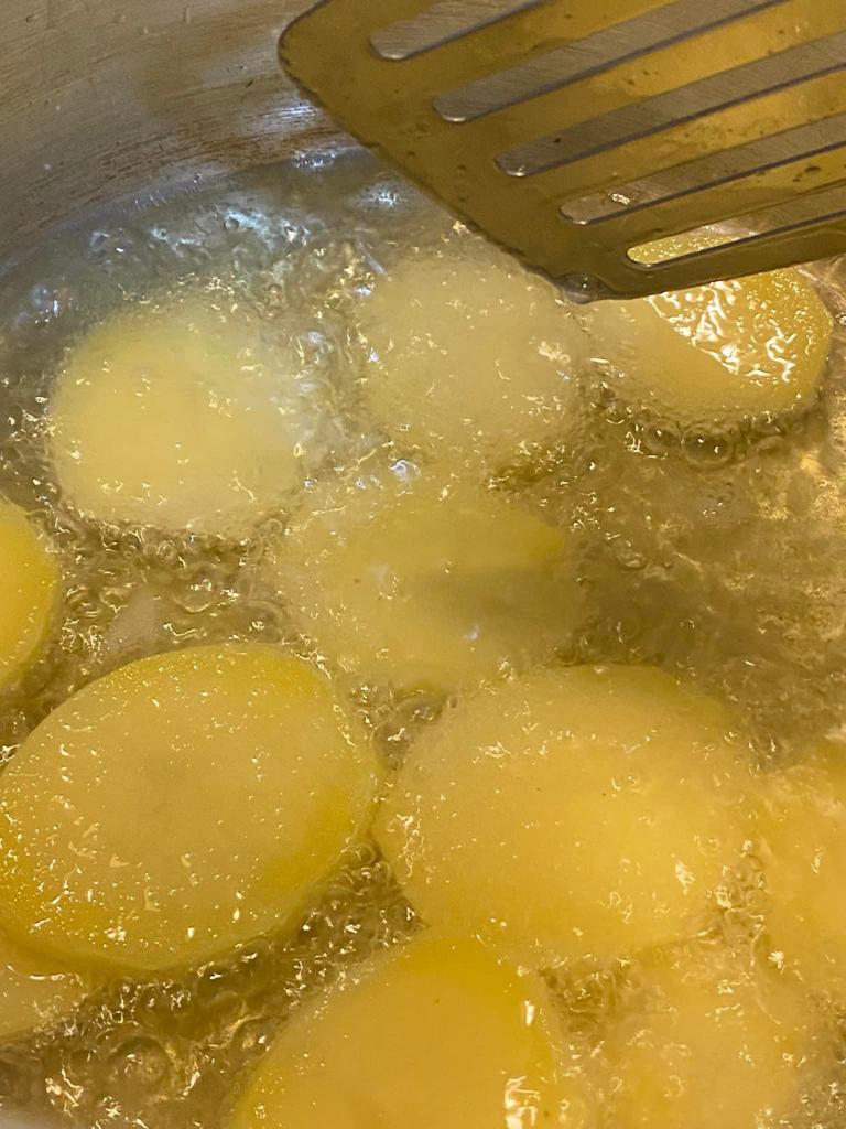 Sliced potatoes frying in hot oil in a deep pan, turning golden and crispy.