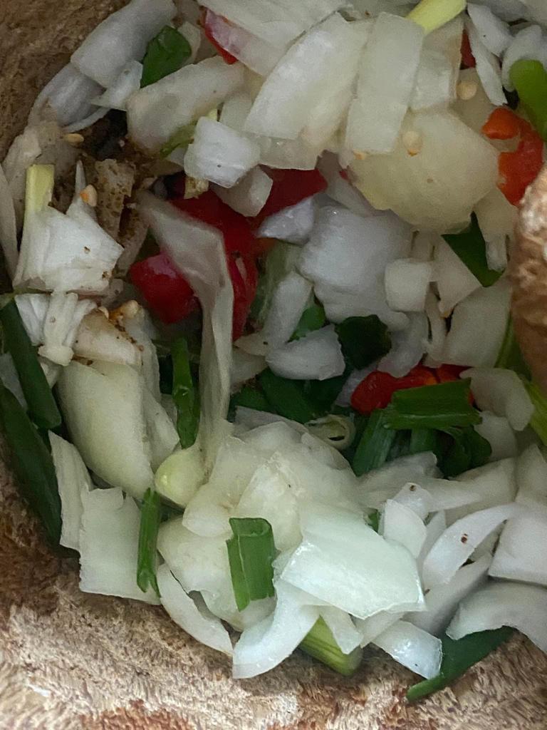 Chopped spring onions, regular onions, and red chilies in a bowl, ready for stew preparation.