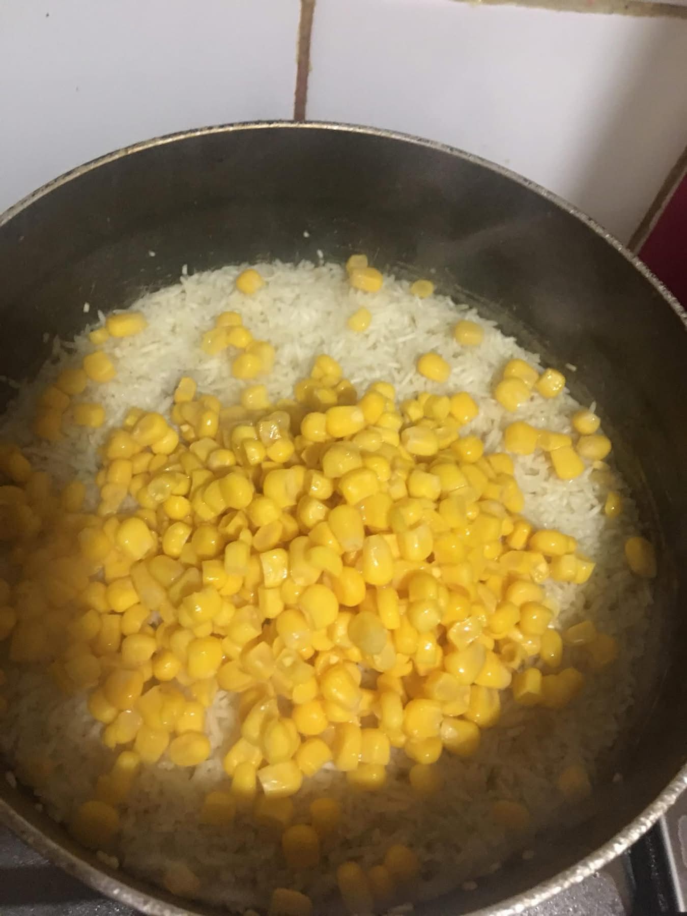 Sweet corn added to fluffy rice in a pot during the final stage of cooking.