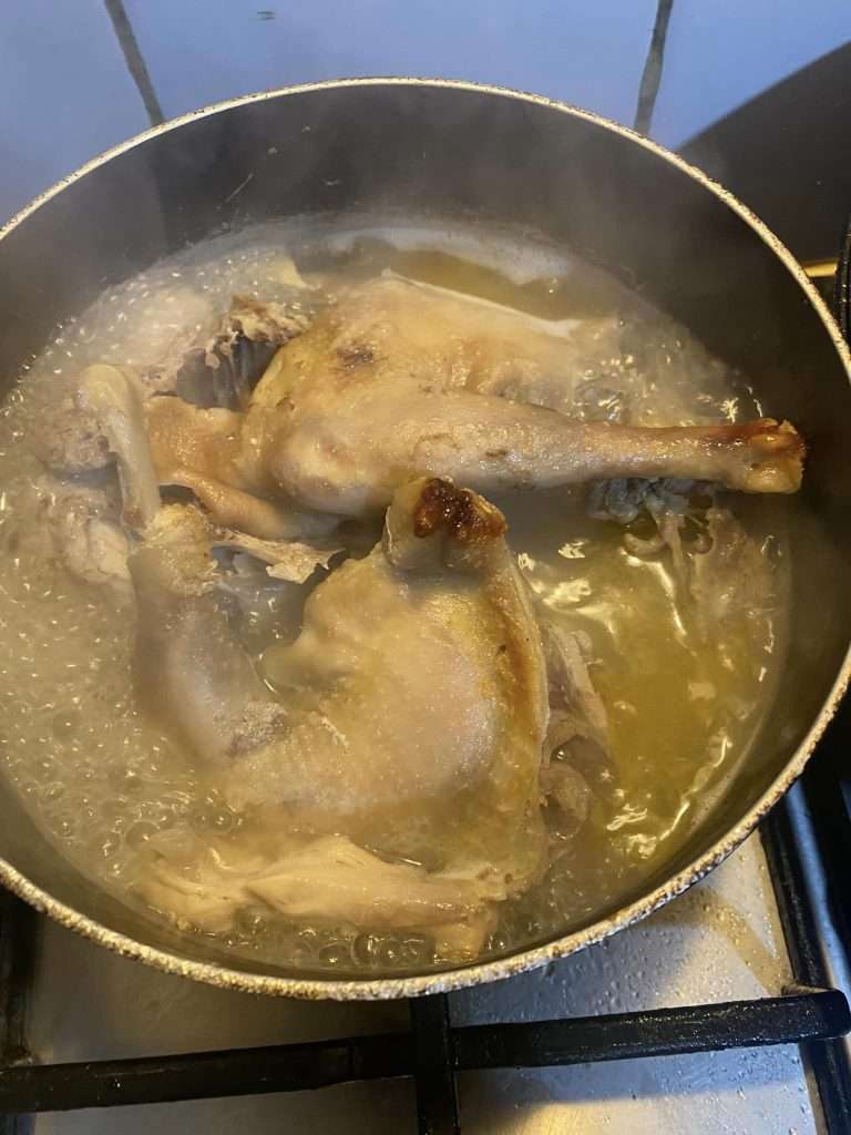 Whole chicken boiling in a pot of water to create broth