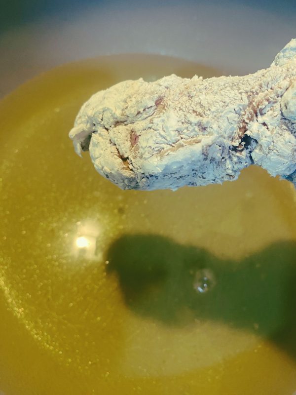 Flour-coated chicken piece about to be placed into hot oil for frying.