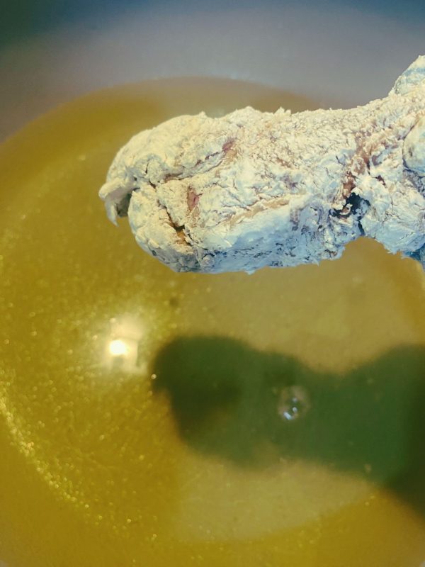 Flour-coated chicken piece about to be placed into hot oil for frying.