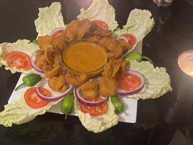 Crispy fried prawns arranged over a fresh salad with tomatoes and lettuce, served with dipping sauce