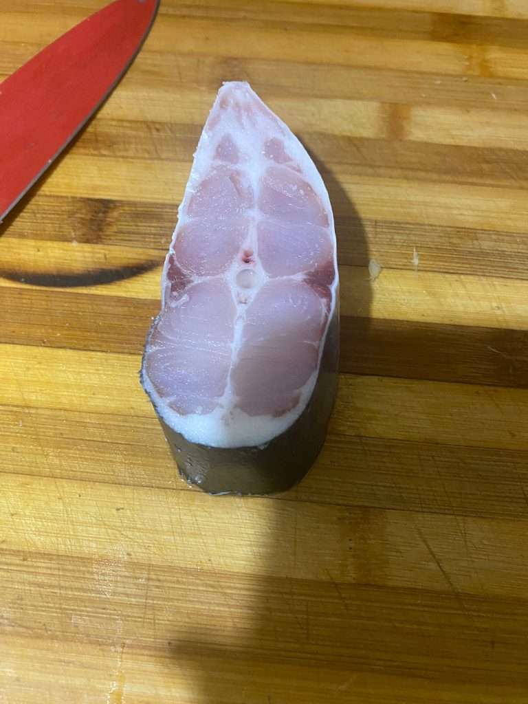 Raw Pangasius steak is placed on a wooden chopping board, ready to be sliced and cleaned.