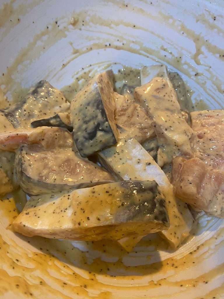 Marinate Pangasius steaks coated with flour, egg, black pepper, and green onions in a mixing bowl.