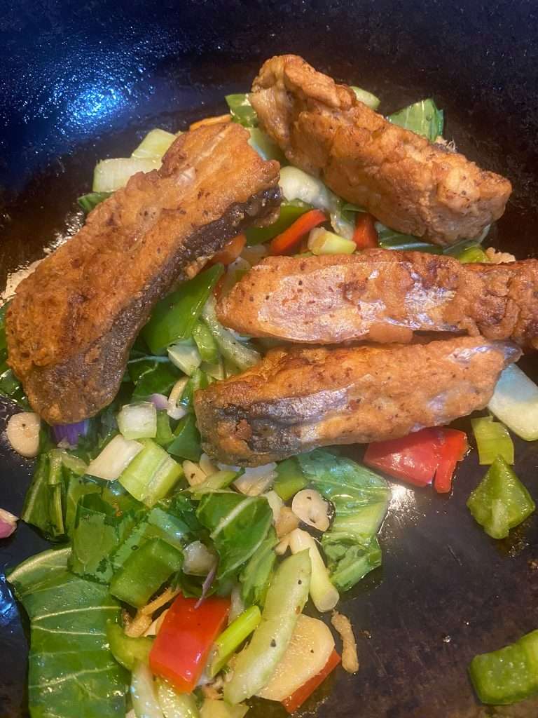 Seared Pangasius steaks with stir-fried vegetables and sauce in a pan.