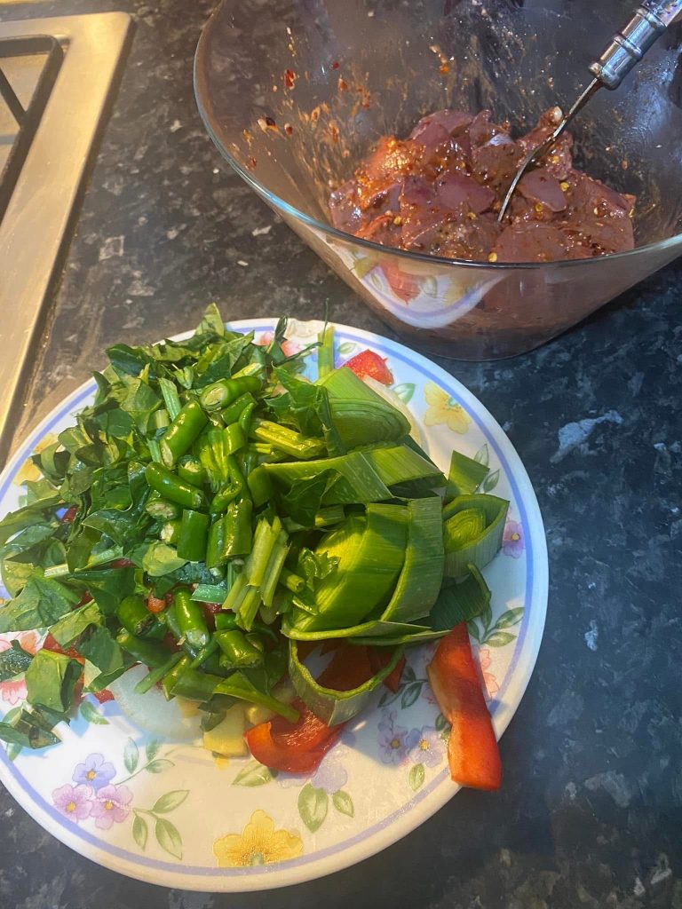 Freshly chopped green vegetables and bell peppers on a plate beside marinated liver in a mixing bowl, ready for the Gourmet Blend recipe.
