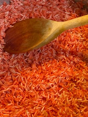 Red-colored rice cooking in a pot with steam rising.