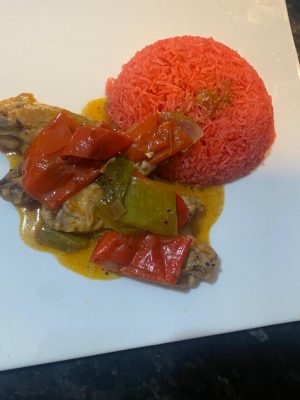 A colorful plate of red rice topped with fried chicken wings and sautéed vegetables.