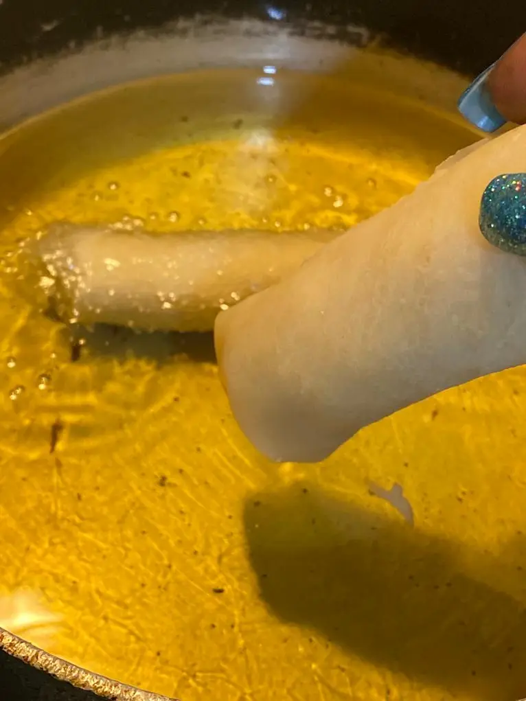 Hand placing a raw spring roll into hot oil for frying