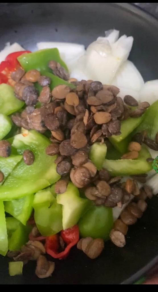 A bowl filled with chopped onions, green bell pepper, red chili, and fermented locust beans ready for blending.