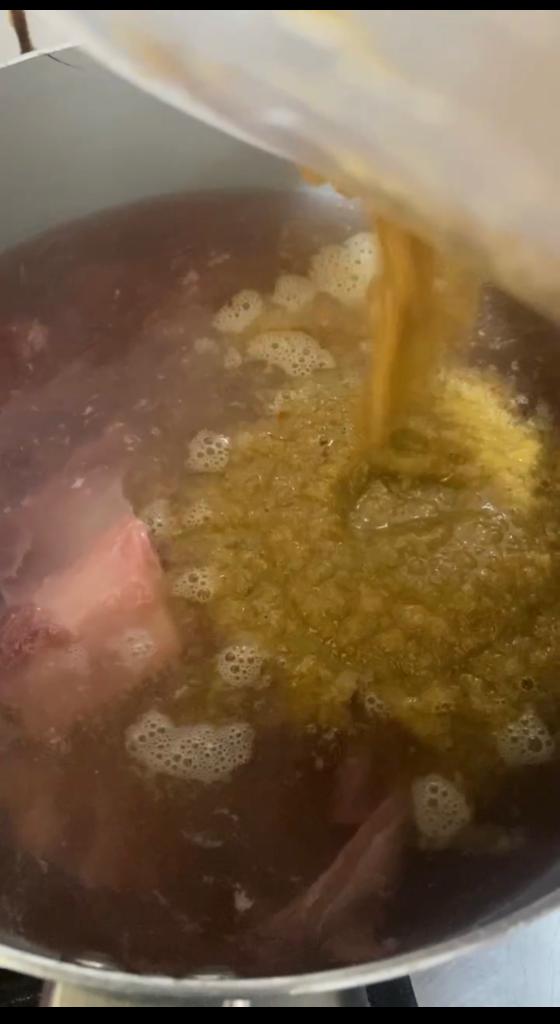 Blended spice mixture being poured over tender meat simmering in a pot.