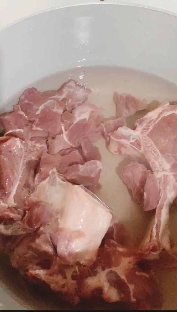 Raw beef and goat meat simmering in a pot of salted water during the initial boiling stage.
