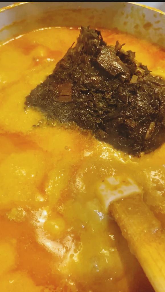 A scoop of shaki and cow belly being added to a thick orange peanut soup.