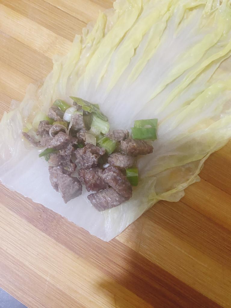 Cabbage leaf filled with seasoned meat and spring onions before rolling into a wrap