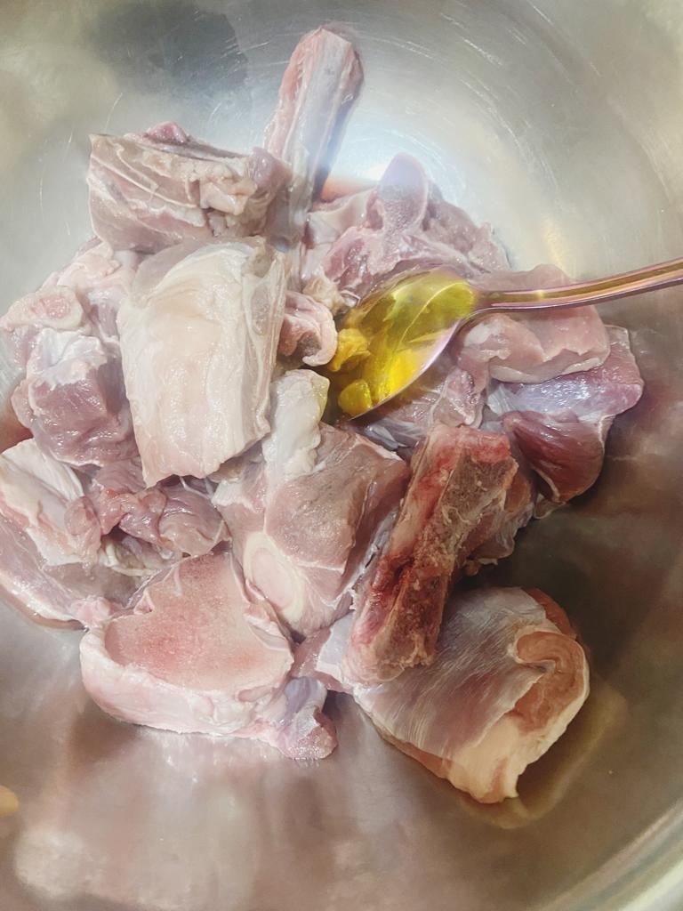 Fresh raw lamb pieces in a mixing bowl with a spoon of oil.