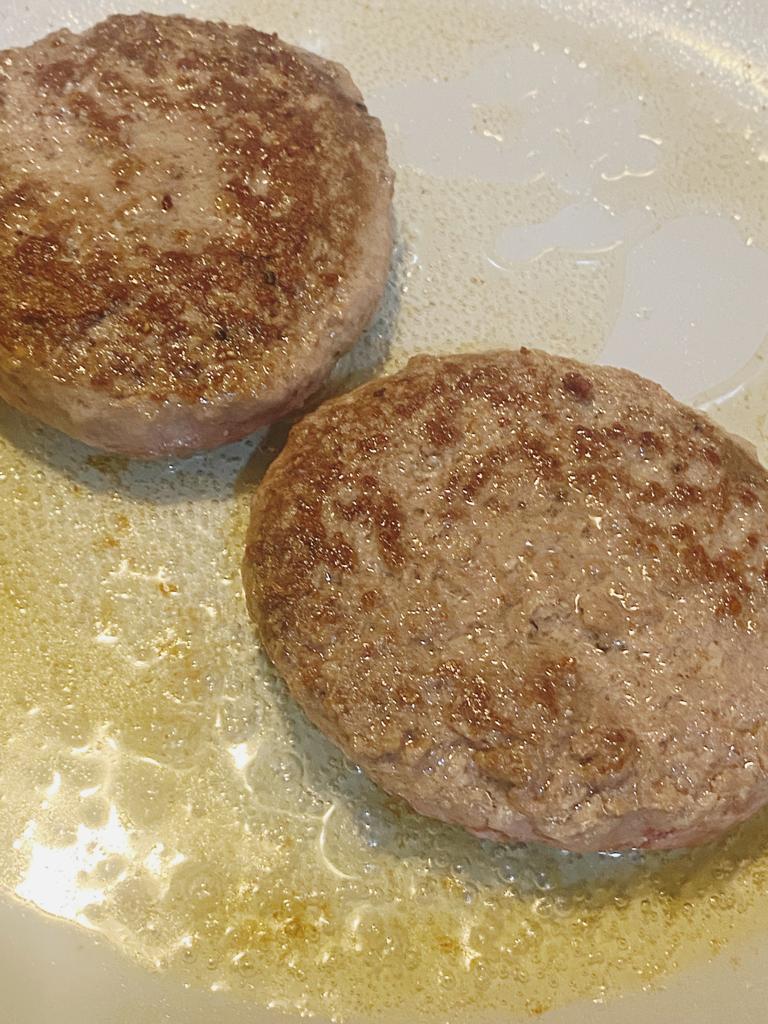 Juicy beef burger patties sizzling in a frying pan.