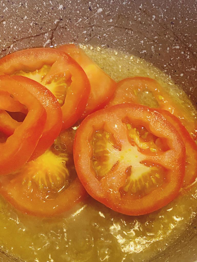 Fresh tomato slices cooking in a pan with oil.