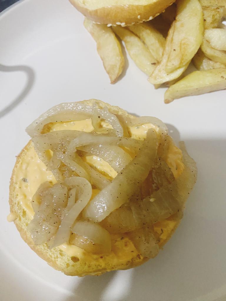 Burger bun with sauce and caramelized onions, served with potato wedges.