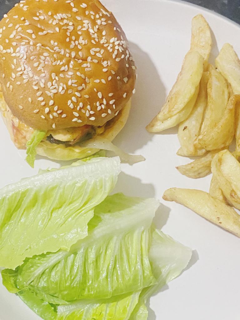 Gourmet beef burger with sesame seed bun, crispy fries, and fresh lettuce on a white plate.