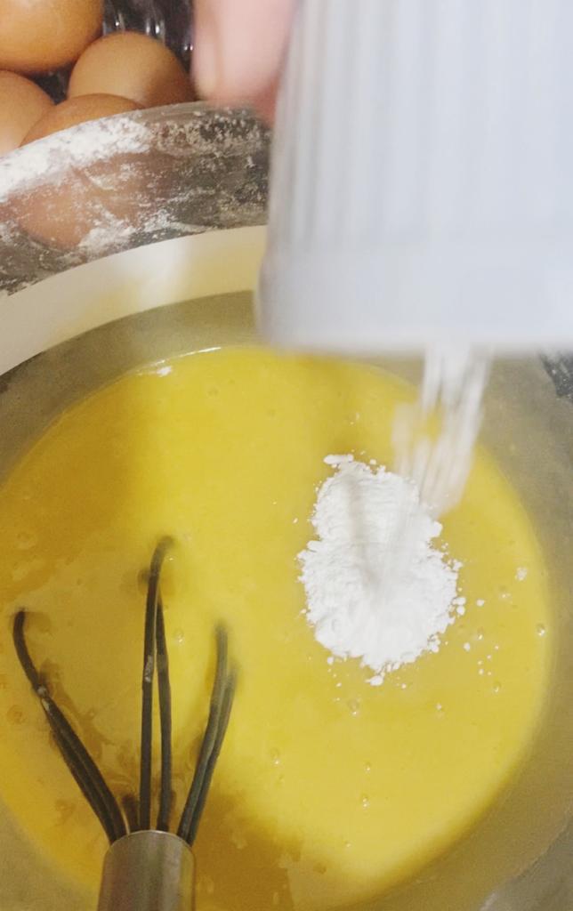 Baking powder is being sprinkled into a yellow cake mixture in a bowl.