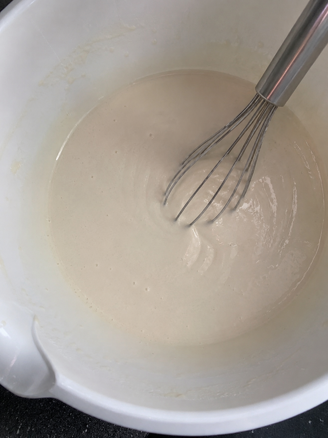 Smooth homemade spring roll batter being whisked in a white mixing bowl