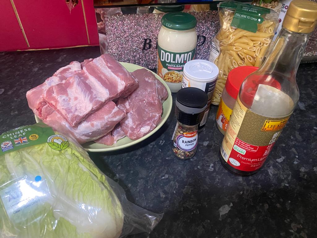 Raw pork ribs on a plate with pasta, Chinese cabbage, pasta sauce, soy sauce, and spices arranged on a kitchen counter