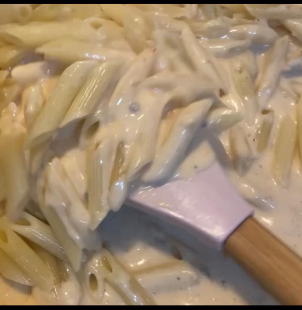 Cooked penne pasta being mixed into creamy sauce.