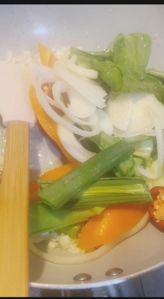 Sliced onions, spring onions, sweet peppers, and okra are cooking in a pan with garlic