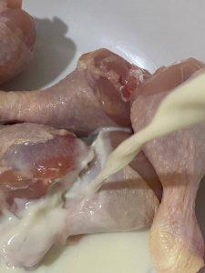 Raw chicken drumsticks are being marinated in fresh milk in a bowl.