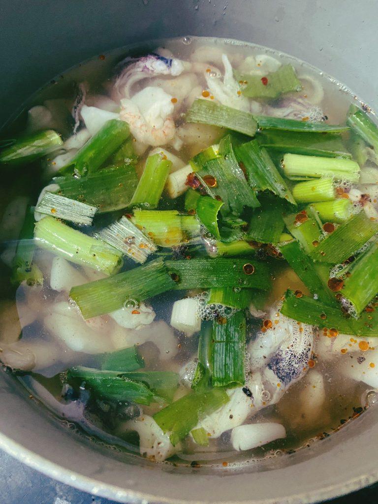 Seafood simmering in a clear broth with spring onions and chili flakes