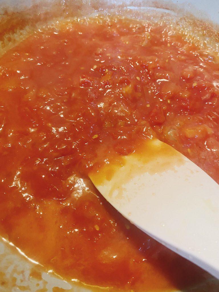 Thickened tomato sauce simmering in a pan with a cornflour slurry.