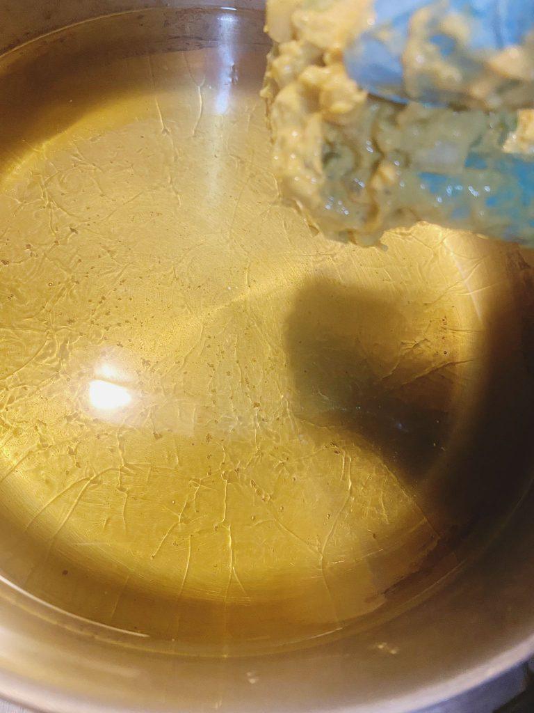 Prawn pakora batter being dropped into hot oil in a pan