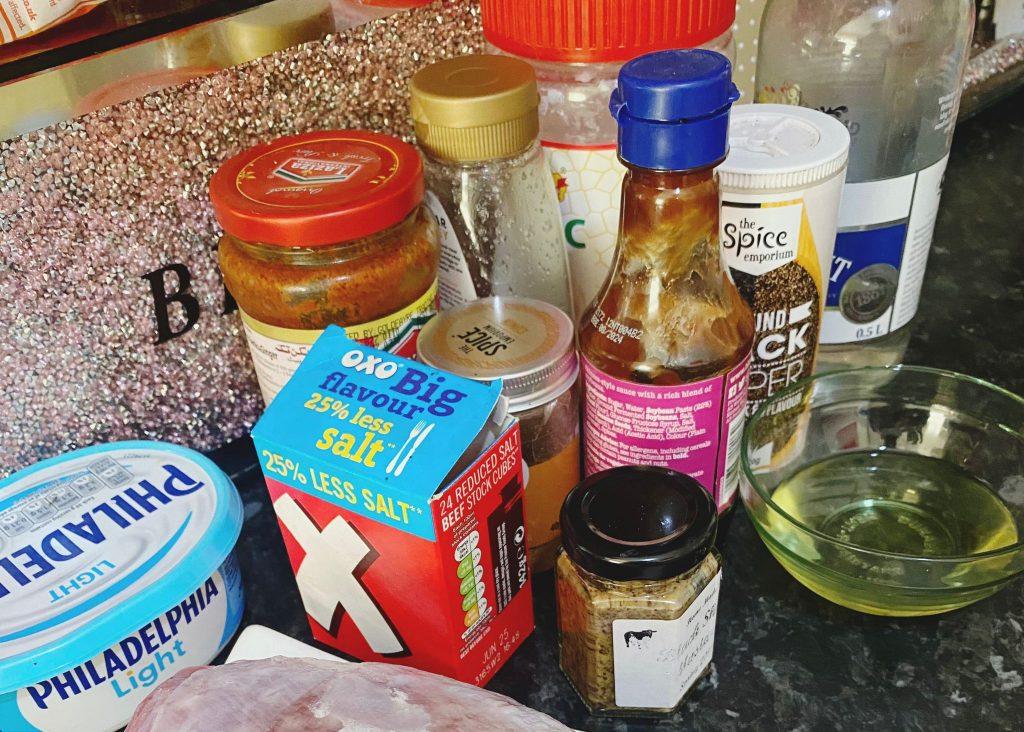 A colorful assortment of marinade ingredients, including spices, sauces, Philadelphia cream cheese, seasoning cubes, vinegar, oil, and honey, neatly arranged on a kitchen counte