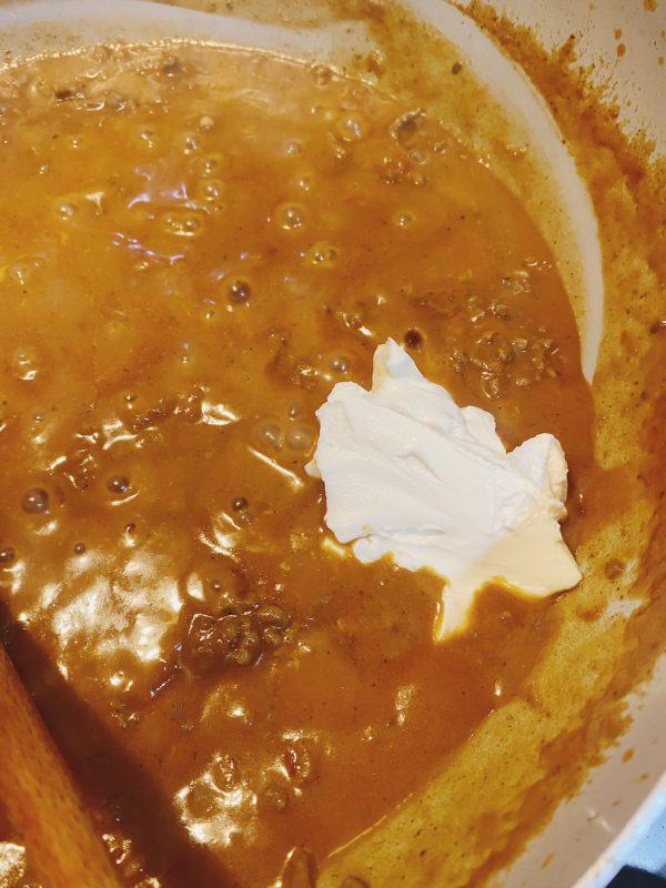 Cream cheese melting into a rich, simmering orange marinade sauce in a pot.