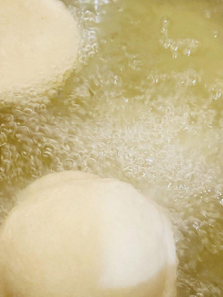 Golden dough rounds frying in a pan, bubbling in hot oil until crispy and puffed.