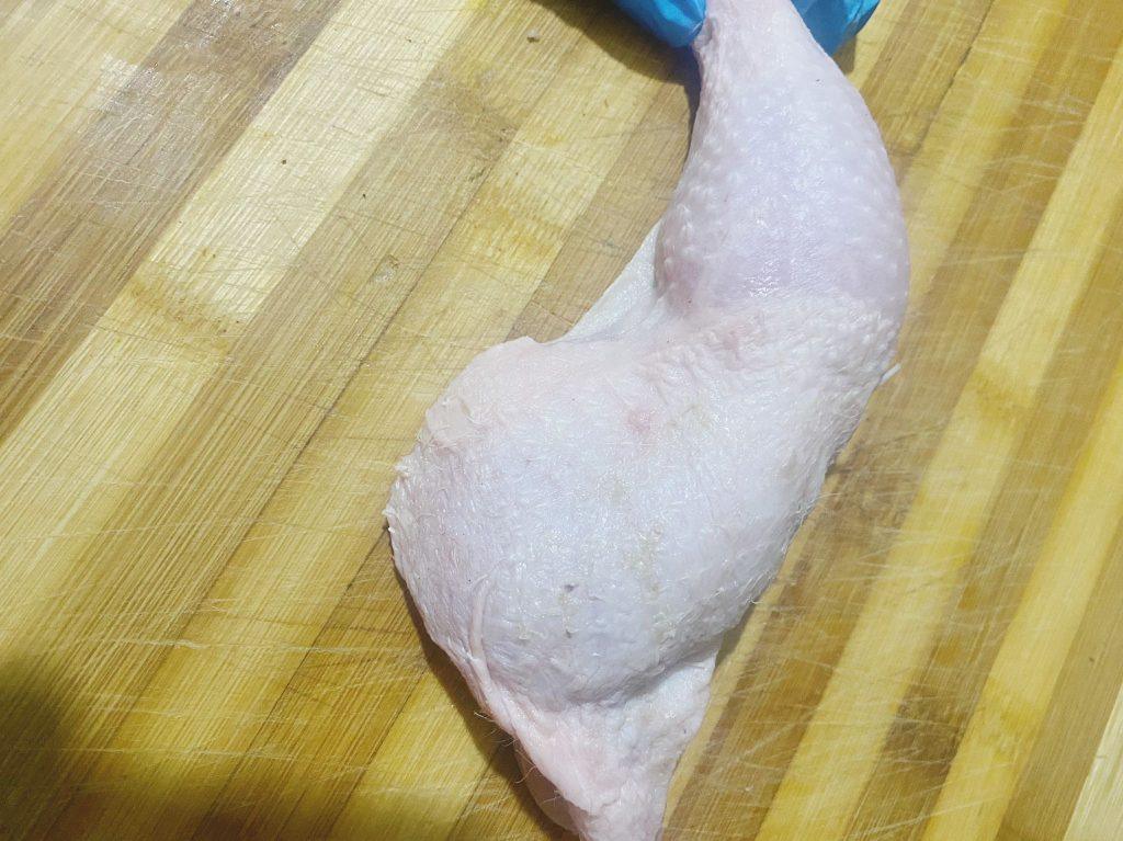 Raw chicken leg placed on a wooden board, ready to be cut into smaller pieces for marinating.