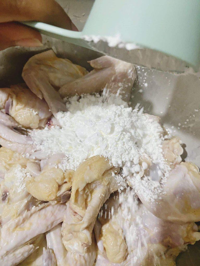 Dusting marinated chicken wings with dry cornflour in a mixing bowl.