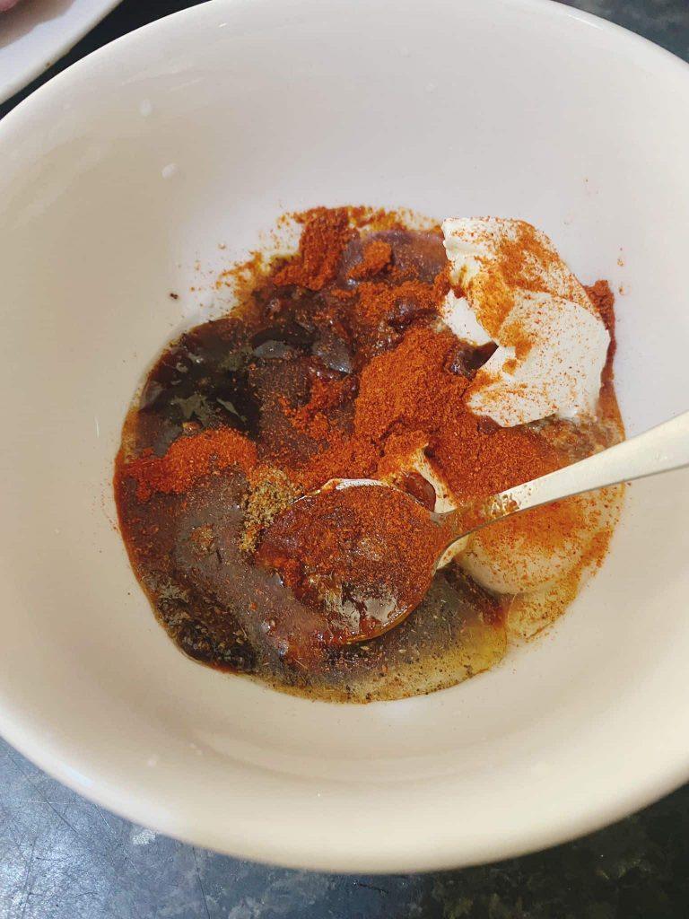 Spices, hoisin sauce, yogurt, and garlic paste in a white bowl before mixing into a marinade.
