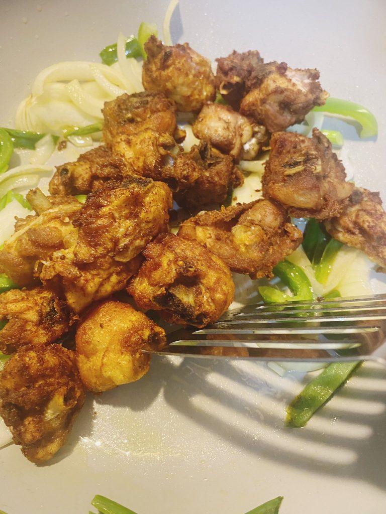 Crispy golden chicken pieces placed on a bed of sliced onions and green peppers, served hot and ready to enjoy.