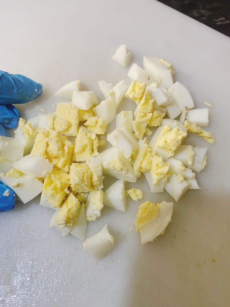 Chopped boiled eggs on a cutting board with a gloved hand beside them