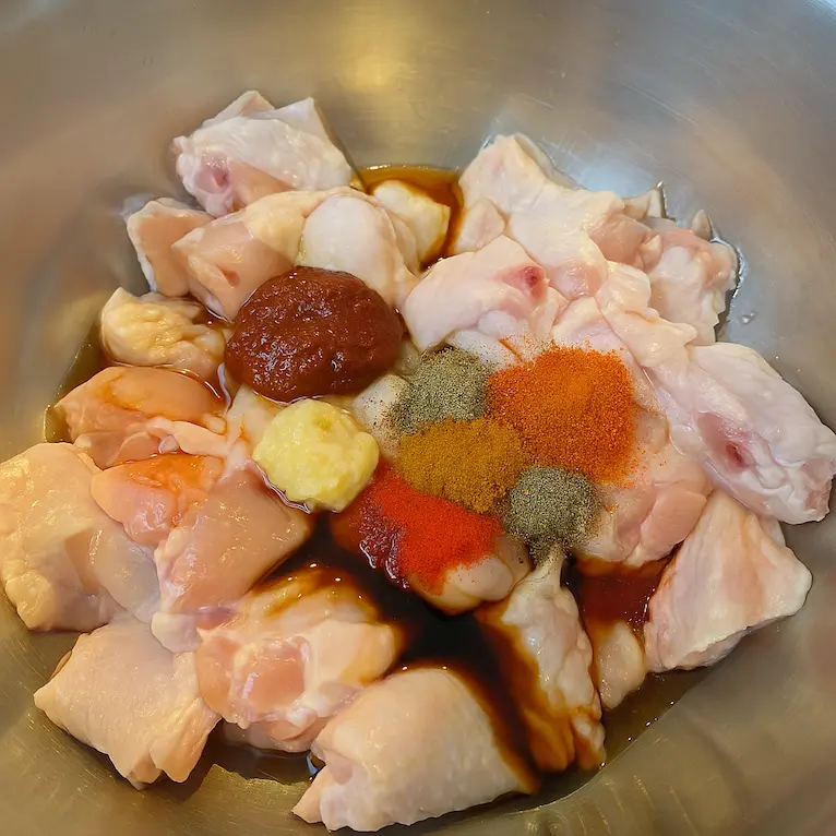 Raw chicken wings marinating in Asian spices inside a metal bowl