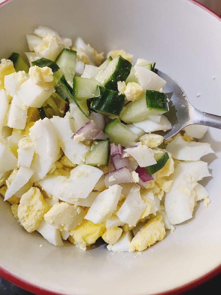 Chopped boiled eggs, cucumber, and onions in a bowl with a spoon